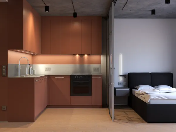 Aneks kuchenny w kształcie litery L z terrakotowymi szafkami do sufitu – za szklaną ścianką sypialnia, betonowy sufit, projekt małej kawalerki w Warszawie.